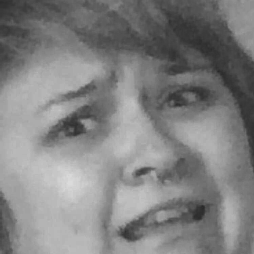 A grainy black and white photograph. An extreme close-up of a white woman's face. The face wears a look of abject terror. This is the face of a person who is not long for this world. This person is Emily Chambers (she/they, light board operator). They will be missed.